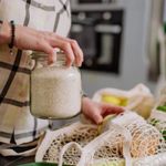 A woman's hand placing a jar of rice into an eco-friendly grocery bag.