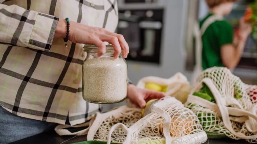 A woman's hand placing a jar of rice into an eco-friendly grocery bag.