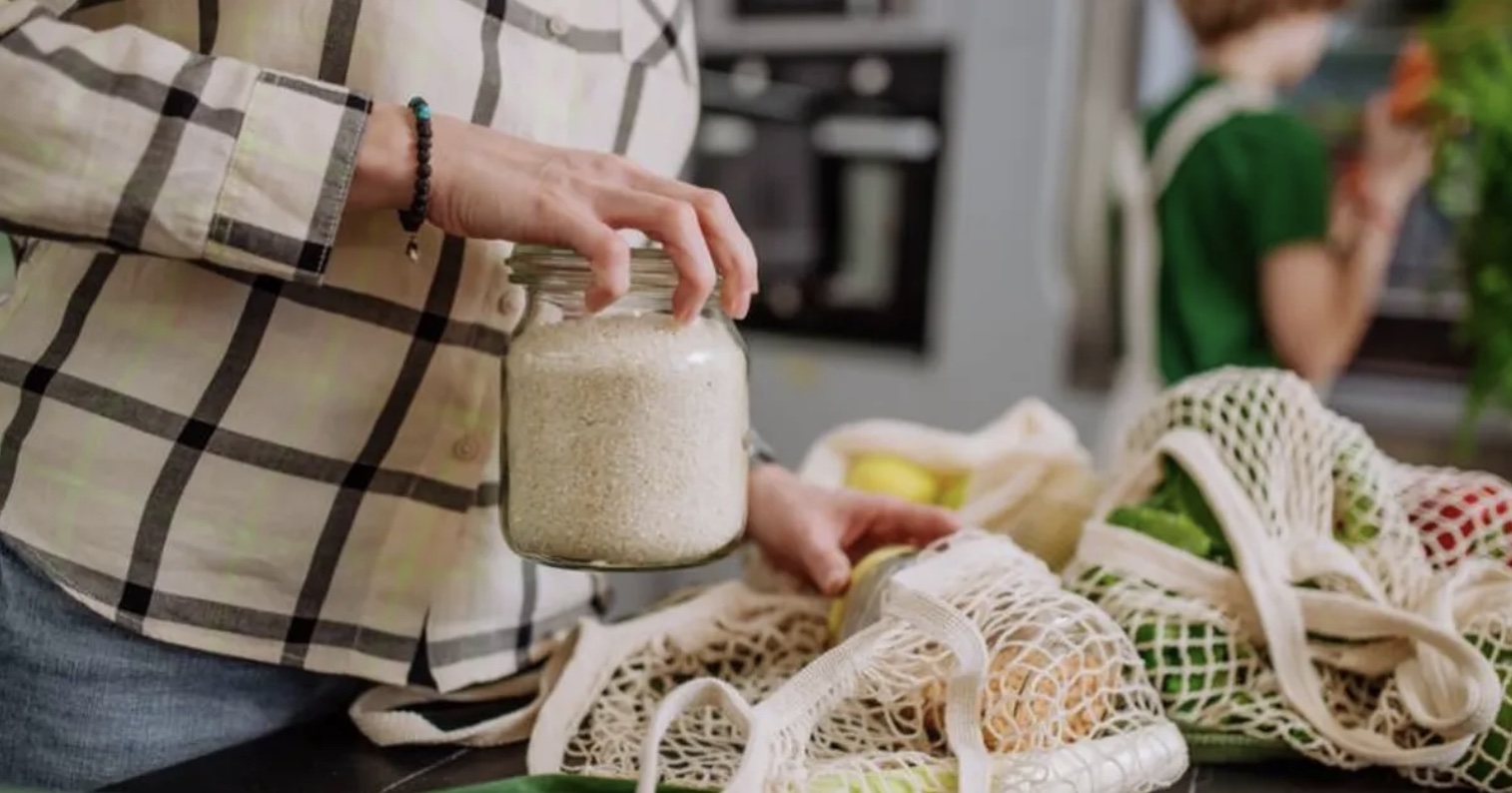 A woman's hand placing a jar of rice into an eco-friendly grocery bag.