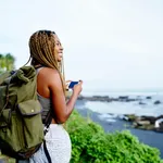 Cheerful Dark Skinned Female Traveller Holding Smartphone Device In Hands