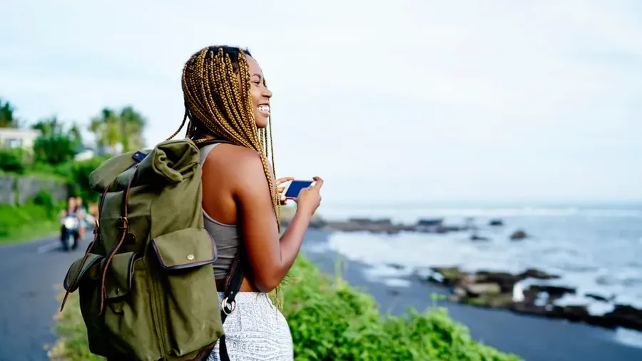 Cheerful Dark Skinned Female Traveller Holding Smartphone Device In Hands