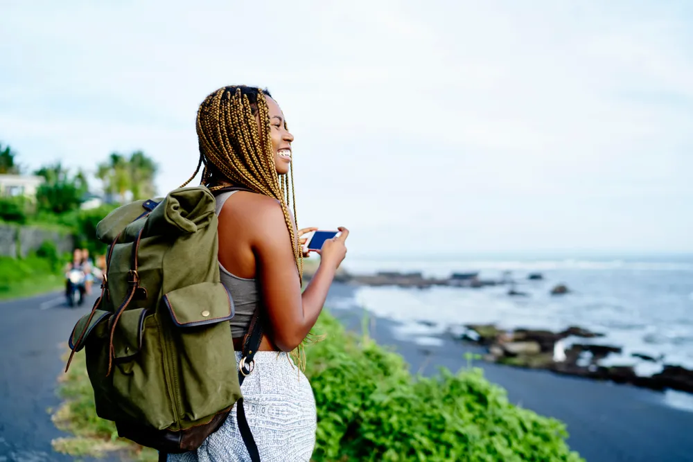 Cheerful Dark Skinned Female Traveller Holding Smartphone Device In Hands