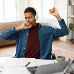 Exhausted Black Teenage Boy In Headphones Yawning Showing Signs Of