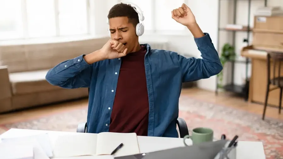 Exhausted Black Teenage Boy In Headphones Yawning Showing Signs Of