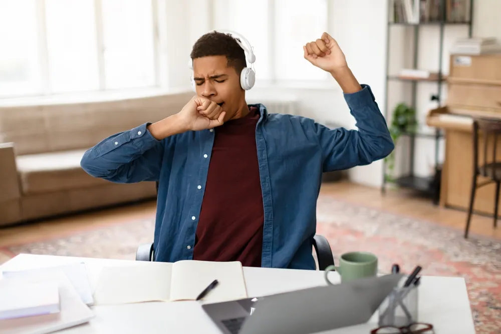 Exhausted Black Teenage Boy In Headphones Yawning Showing Signs Of