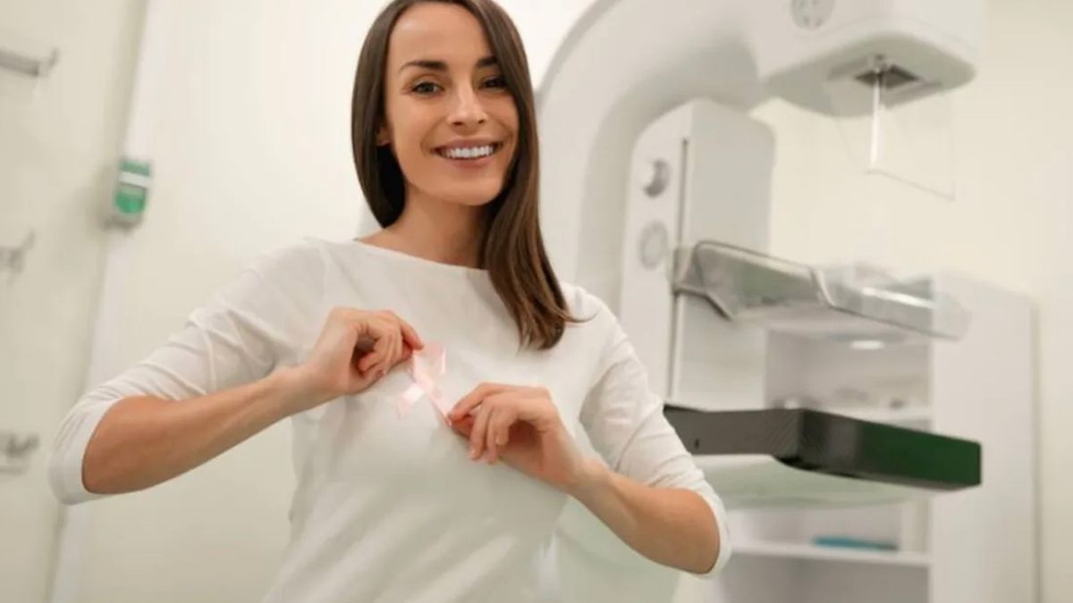 A woman in a hospital gown putting on a pink breast cancer ribbon.