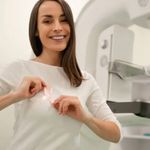 A woman in a hospital gown putting on a pink breast cancer ribbon.